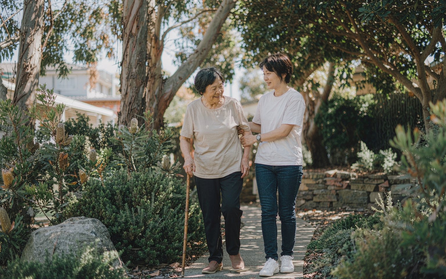 A support worker and an older woman walking together in a native garden