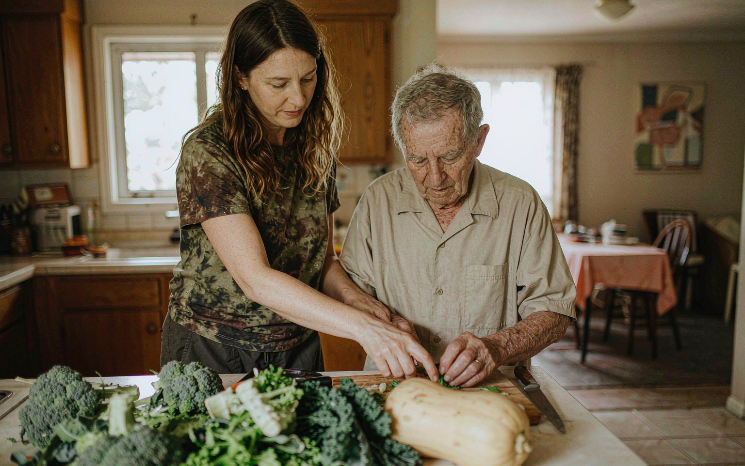 A support worker helping an older man prepare vegetables at his kitchen bench
