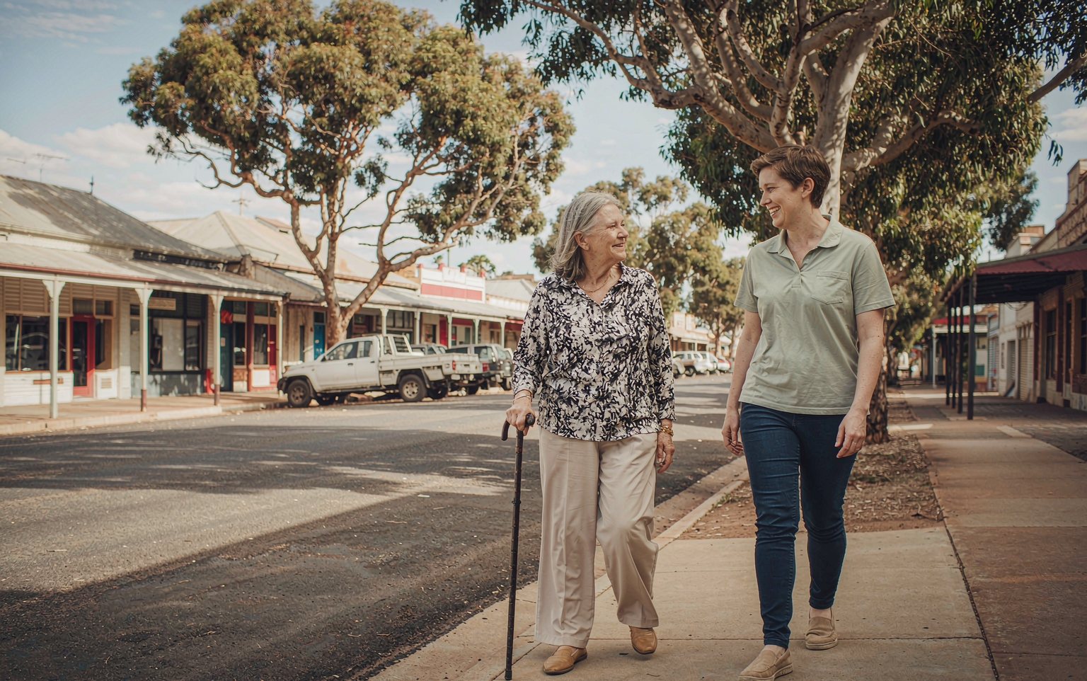 A support worker walking with an older woman along the main street of a wheatbelt town